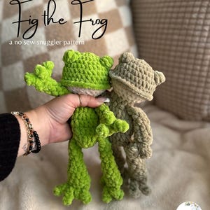May include: Two crocheted frog plushies. One is bright green, the other is tan. The green frog is held up, showing its arms and legs. The text "Fig the Frog" and "a no sew snugger pattern" are above the frogs.