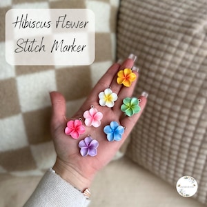 Peut inclure: Plusieurs marqueurs de point en forme de fleurs d'hibiscus colorées. Les marqueurs sont de différentes couleurs, notamment rose, jaune, blanc, vert, bleu et violet. Le texte "Hibiscus Flower Stitch Marker" est visible.