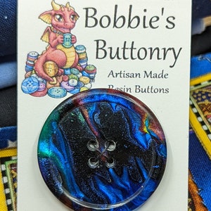 Op de afbeelding: Een blauwe, zwarte en rode harsknop met een swirl-patroon. De knop heeft vier gaten en is handgemaakt.