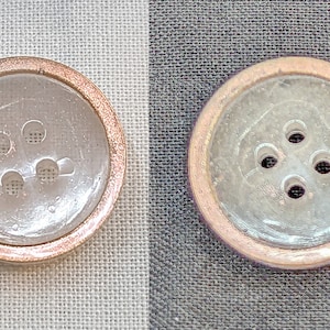 Op de afbeelding: Een close-up van een doorzichtige plastic knoop met een gouden rand. De knoop heeft vier gaten in een cirkelvormig patroon.