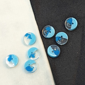 Op de afbeelding: Assortiment van blauwe en witte knopen met een swirl-ontwerp. De knopen zijn gemaakt van glas en hebben een glanzende afwerking.