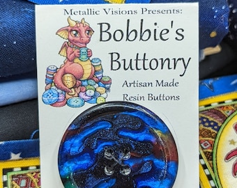 May include: A blue and black resin button with a swirling pattern. The button is on a white card with the text "Metallic Visions Presents: Bobbie's Buttonry Artisan Made Resin Buttons".