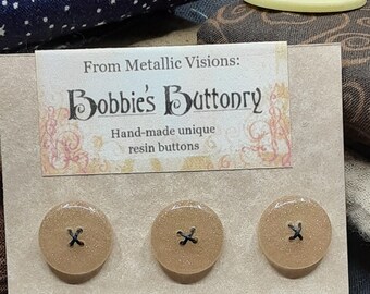 Puede incluir: Tres botones de resina marrón con un diseño en X negro. Los botones se muestran en una tarjeta con el texto "From Metallic Visions: Bobbie's Buttonry Hand-made unique resin buttons".
