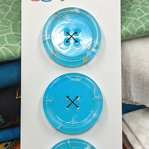 May include: Three turquoise blue resin buttons with a white swirl design and black stitching. The buttons are displayed on a white card with the text "Metallic Visions Presents: Bobbie's Buttonry Artisan Made Resin Buttons".