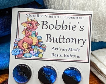 May include: Three artisan-made resin buttons with a black and blue galaxy design. The buttons are round with two holes for sewing. The card reads "Bobbie's Buttonry" with a cartoon dragon illustration.