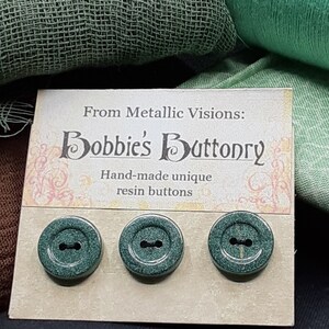 Op de afbeelding: Drie groene harsknoppen met een glinsterende afwerking. De knoppen worden getoond op een kaart met de tekst "From Metallic Visions: Bobbie's Buttonry Hand-made unique resin buttons".