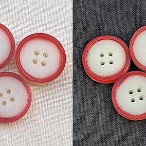 Op de afbeelding: Vijf witte knoppen met een rode rand. Elke knop heeft vier gaten.