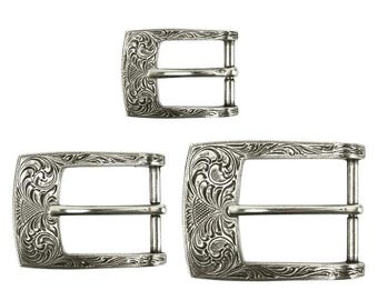 May include: Three silver-colored belt buckles with an ornate floral design. The buckles are rectangular with a central bar for the belt strap. The sizes vary, with one small and two larger buckles.