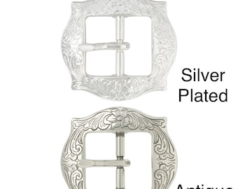 Könnte beinhalten: Zwei silberfarbene Gürtelschnallen mit einem gravierten Blumenmuster. Die obere Schnalle ist mit "Versilbert" und die untere Schnalle mit "Antiksilber" beschriftet. Beide Schnallen sind 25 mm (1 Zoll) groß.