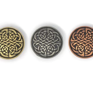 Puede incluir: Tres botones redondos de metal con diseños de nudos celtas. Los botones son de color oro, plata y cobre. El intrincado trabajo de nudos es el punto focal de cada botón, creando una apariencia detallada y texturizada.