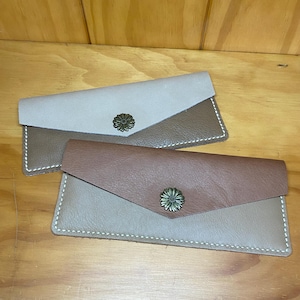 May include: Two leather wallets in a brown and beige colour scheme. Each wallet features a decorative flower-shaped button.