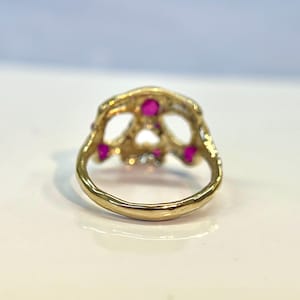 May include: Gold skull ring with pink gemstones. The ring is detailed with a textured finish and has a wide band.