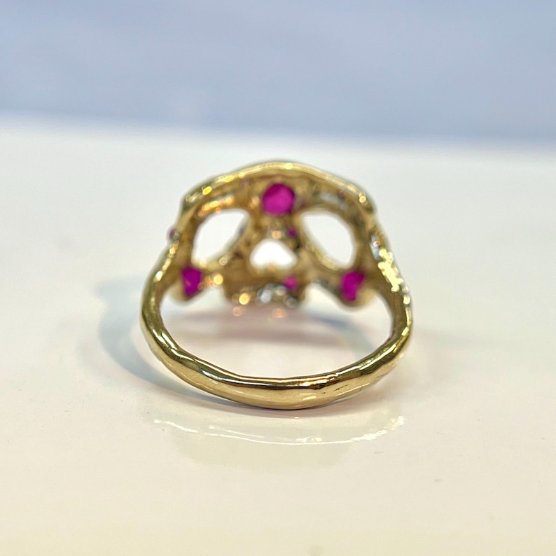 May include: Gold skull ring with pink gemstones. The ring is detailed with a textured finish and has a wide band.