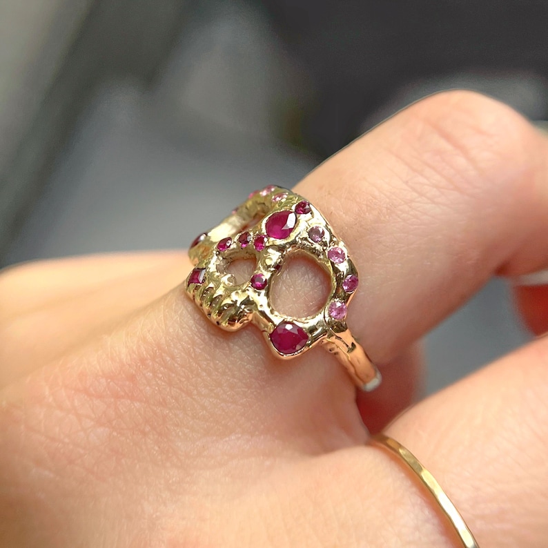 May include: A gold ring with a skull design, set with small red and pink gemstones.