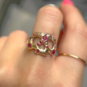 May include: A gold ring shaped like a skull with red and pink gemstones.