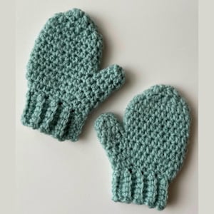 May include: A pair of crocheted baby mittens in a light green colour. The mittens have a simple stitch pattern and a ribbed cuff.