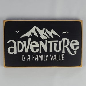 May include: Black wooden sign with a white mountain silhouette and the text "adventure is a family value".