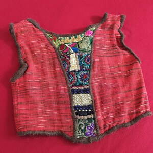 May include: A red sleeveless vest with a brown trim and colorful embroidered patches on the back.