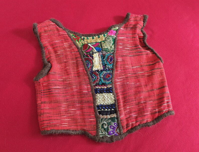 May include: A red sleeveless vest with a brown trim and colorful embroidered patches on the back.