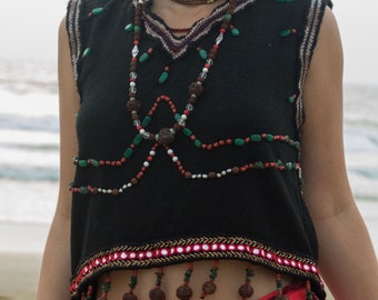 May include: A black sleeveless top with a beaded neckline and fringe trim. The top is decorated with beads, stones, and other embellishments. The model is wearing a red skirt.