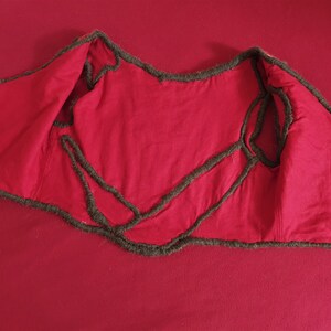 May include: Red vest with brown trim. The vest is turned inside out, showing the stitching and lining.