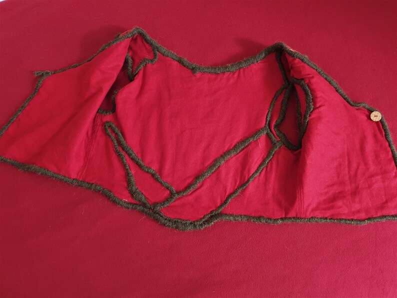 May include: Red vest with brown trim. The vest is turned inside out, showing the stitching and lining.