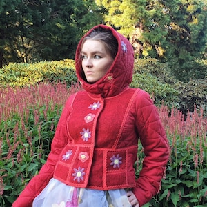 May include: A red quilted jacket with a hood and floral embroidery. The jacket has a high collar and a button closure. The embroidery is in shades of pink, purple, and yellow.