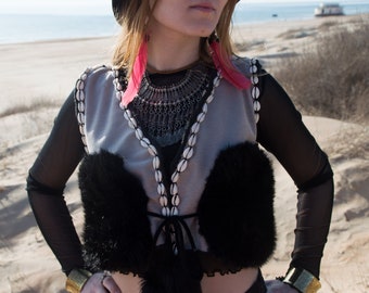 May include: A gray vest with a black fur trim and a white shell necklace. The vest has a tie closure and is worn over a black mesh top.