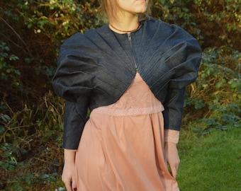 May include: A denim jacket with puffed sleeves and a cropped length. The jacket is unbuttoned and has a zipper closure. The model is wearing a pink dress underneath the jacket.