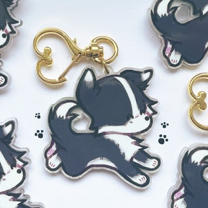 May include: Five black and white cartoon dog charms with gold heart-shaped keychains. The charms are made of acrylic and feature a cute, stylized design.