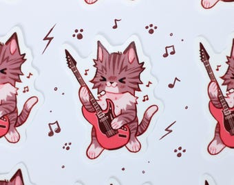May include: A sticker featuring a cartoon grey tabby cat with a white chest playing a bright red electric guitar. The cat has closed eyes and a happy expression. Surrounding the cat are small dark brown musical notes, paw prints, and lightning bolt symbols.