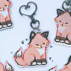 Puede incluir: Una colección de llaveros de acrílico transparente con un diseño de zorro de dibujos animados. El zorro está representado en tonos melocotón, marrón y rojo, en posición sentada. Cada llavero tiene un cierre plateado en forma de corazón. Huellas de patas dispersas.