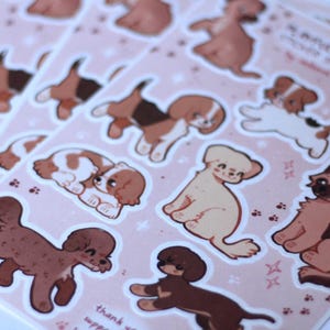 May include: A sheet of stickers featuring various dog breeds in a cartoon style. The stickers are on a pink background with white stars and paw prints. The text "So many pups, so little time" is at the top of the sheet.