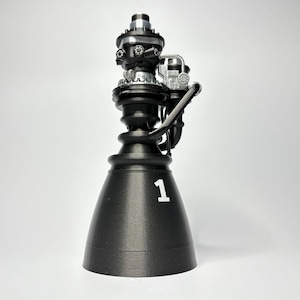 May include: A black and silver 3D printed model of a rocket engine with the number 1 printed on the side.