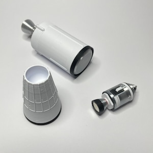 K&ouml;nnte beinhalten: Drei wei&szlig;e Plastikteile f&uuml;r ein Modellraketen-Set. Das gr&ouml;&szlig;te Teil ist ein zylindrischer K&ouml;rper mit einem schwarzen Ring am oberen Ende. Das zweite Teil ist ein kegelf&ouml;rmiger Nasenkonus. Das dritte Teil ist ein kleineres zylindrisches Teil mit einem schwarzen Ring am oberen Ende und einer silbernen Spitze.