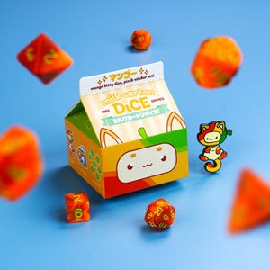 May include: A set of orange dice and a milk carton-shaped box with the text "milk carton DICE" and Japanese text. A pin of a cat is also included. The box has a cute cat face design and the words "mango kitty dice, pin & sticker set!"