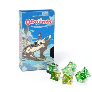May include: A blue game box titled "Obojima" featuring a shark-like creature illustration. Several green and clear dice with white numbers are scattered in front of the box. The box has a cartoon-style illustration.