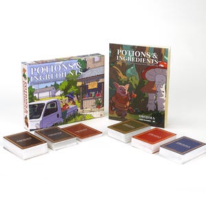 May include: A board game box and book titled "Potions & Ingredients" with colorful illustrations. Several decks of cards are in front of the box and book. The box shows a white truck and a shop. The book cover features a pig and mushroom.