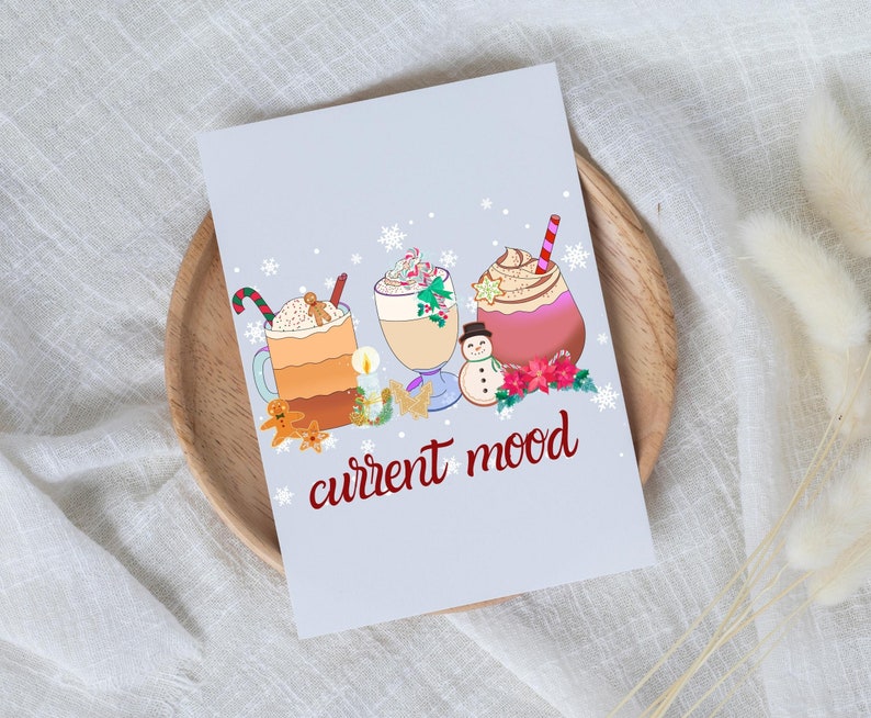 May include: A light blue card with a wintery scene of three mugs of hot chocolate with whipped cream and toppings. The text "current mood" is written in red below the mugs.