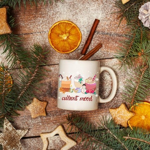 May include: White ceramic mug with a winter-themed design featuring three mugs of hot beverages with whipped cream and toppings. The mug has the text "current mood" printed on the front.
