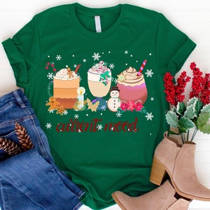 May include: Green t-shirt with a Christmas-themed design featuring three mugs of hot chocolate with whipped cream and candy canes, a snowman, and the text "current mood".