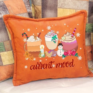 May include: Orange throw pillow with a festive design featuring three mugs of hot chocolate topped with whipped cream and candy canes. The text "current mood" is printed in red on the pillow.