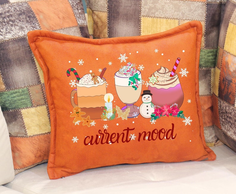 May include: Orange throw pillow with a festive design featuring three mugs of hot chocolate topped with whipped cream and candy canes. The text "current mood" is printed in red on the pillow.