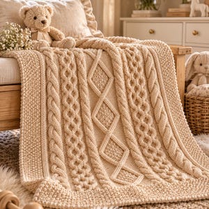May include: A cream-colored knitted blanket featuring a central diamond pattern flanked by vertical cable knit columns and a textured seed stitch border. The blanket is draped over a wooden surface, showcasing intricate yarn work and a soft, uniform neutral tone throughout the entire textile piece.