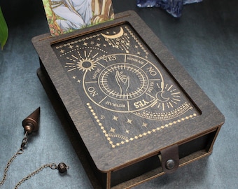 May include: A wooden box with a sliding lid, featuring a gold-colored design of a pendulum chart with the words "YES", "MAYBE", "NO", and "TRY AGAIN".