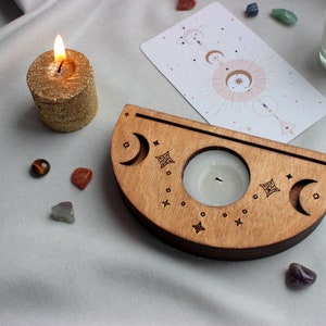 May include: Wooden candle holder with a crescent moon design and a small candle in the center. The holder is surrounded by crystals and a card with a celestial design.