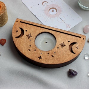 May include: A wooden crescent moon candle holder with two candle wells and a decorative design of moons and stars. The holder is made of light brown wood and has a natural finish.