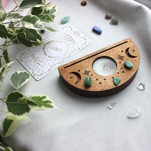 May include: A wooden crescent moon candle holder with a small white candle in the center. The holder is decorated with green stones and moon phases.