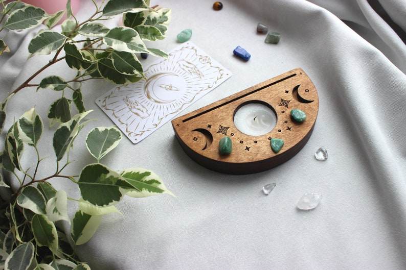 May include: A wooden crescent moon candle holder with a small white candle in the center. The holder is decorated with green stones and moon phases.