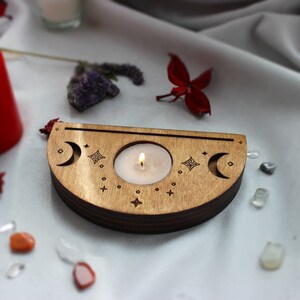 May include: A wooden candle holder with a crescent moon design and stars. A small white candle is burning in the center of the holder.